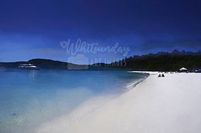 An elevated dusk view over a turquoise bay and white beach with a boat and two people silhouetted on the sand.