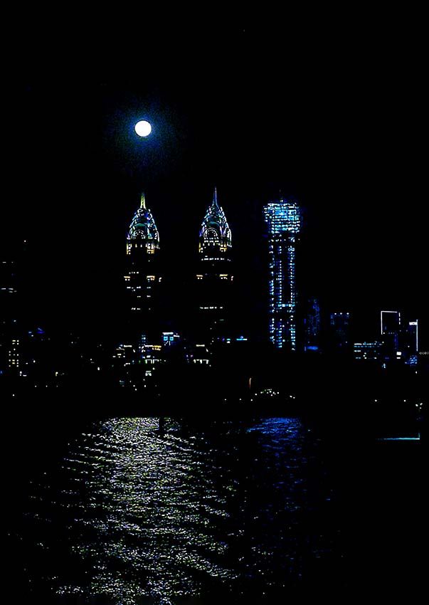 A full moon rising above illuminated Dubai skyscrapers, reflected in the water at night.