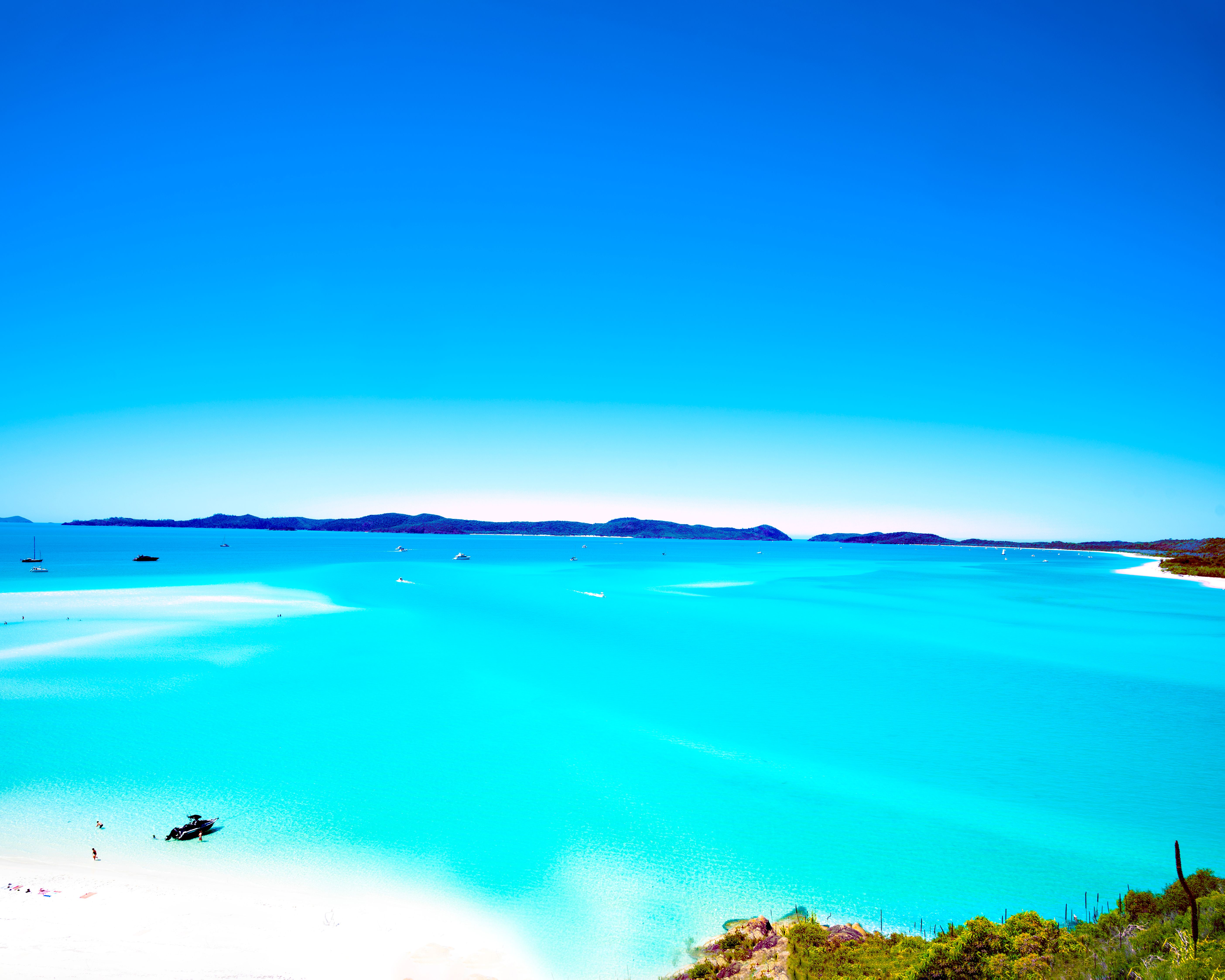 An elevated view over swirling turquoise water and Whitehaven Beach's white sand from the lookout, with boats and swimmers below.