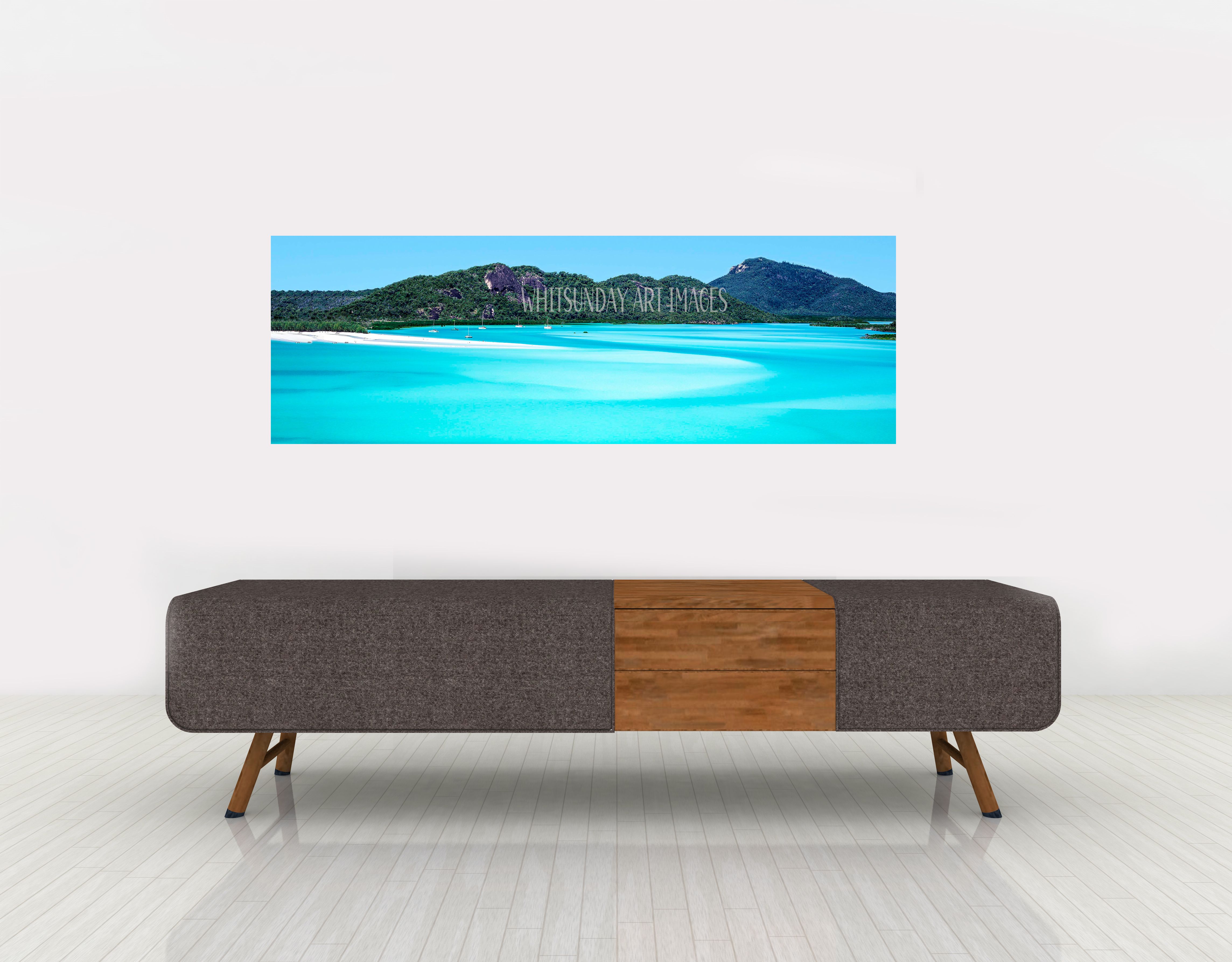 A wide panoramic print of Hill Inlet's turquoise water and headland hangs above a bench seat in a plain white room.