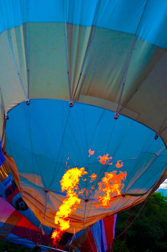 Close-up of a hot air balloon's burner flame lighting up the envelope against a dusk sky.