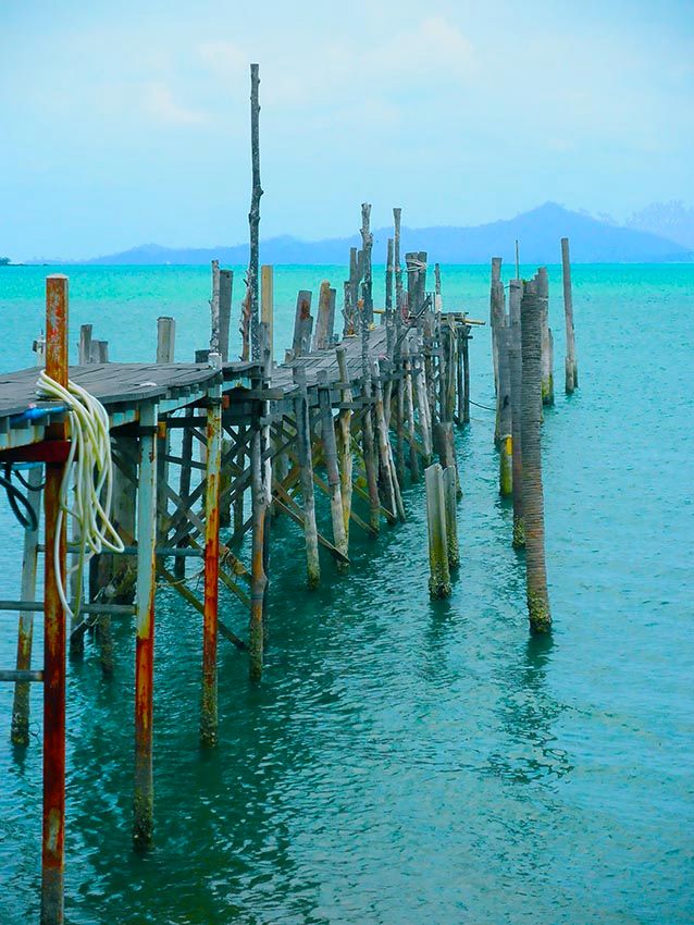 A weathered wooden jetty stretching into turquoise water at Koh Samui, Thailand.