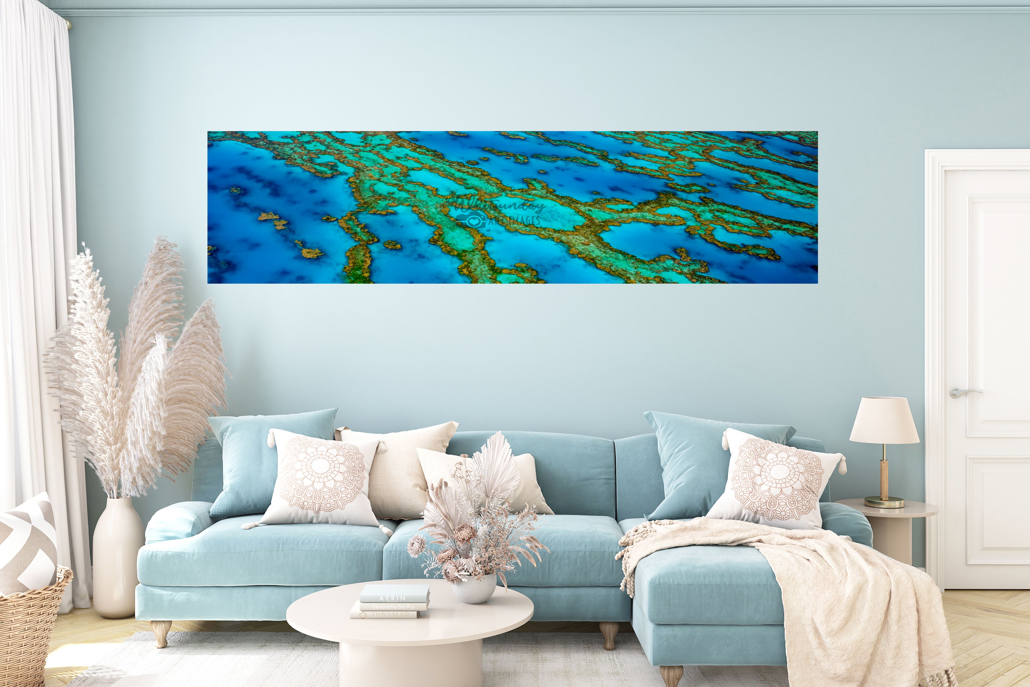 A wide aerial reef panorama print hangs above a pale blue sofa in a living room.
