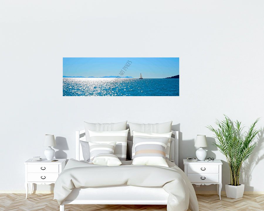 A panoramic photo of a lone yacht sailing across sun-sparkled water, displayed above a white bed.