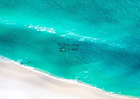 Aerial close-up of turquoise water meeting a white sand beach edge.