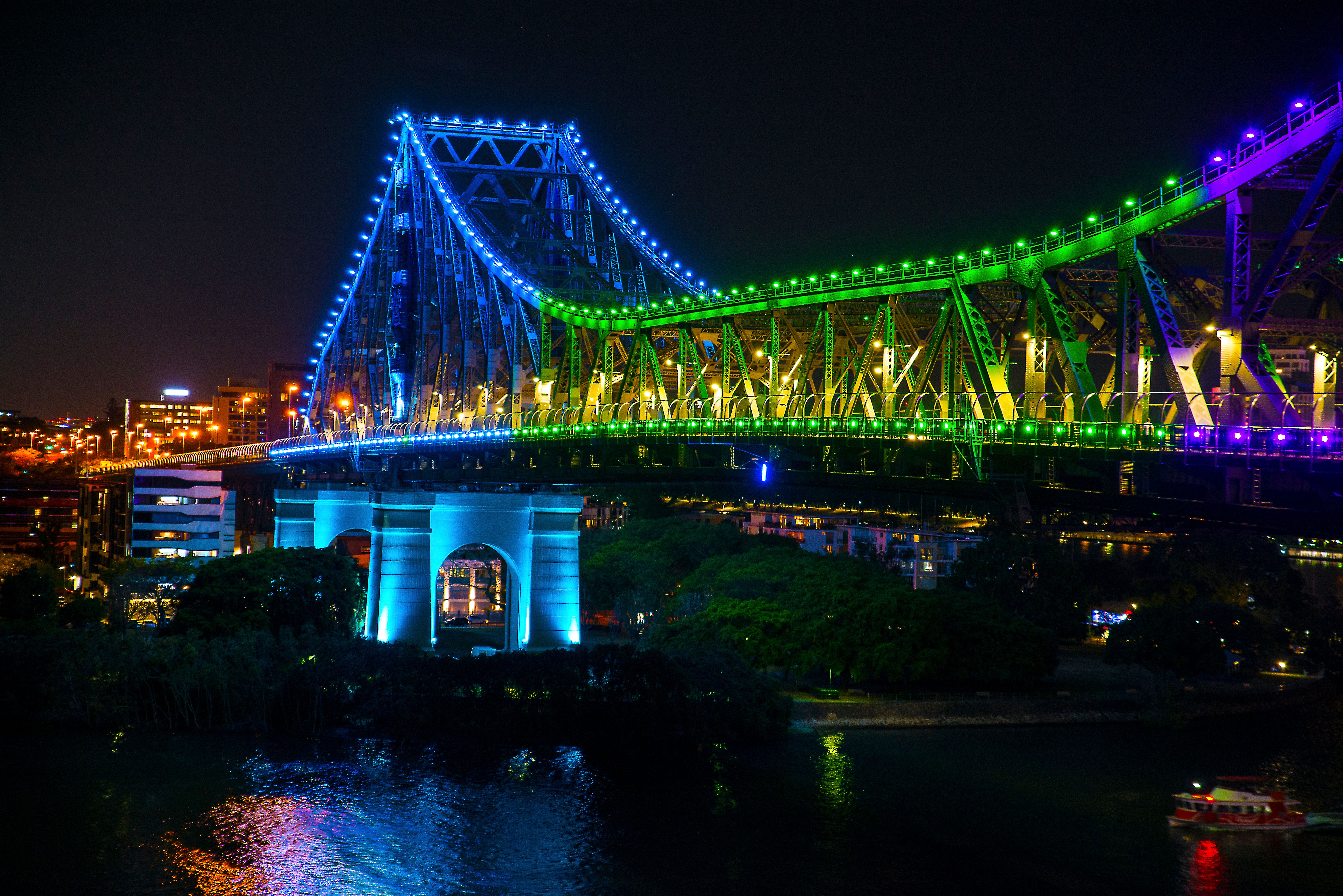 The Story Bridge in Brisbane lit in blue and green at night, reflected in the river below.
