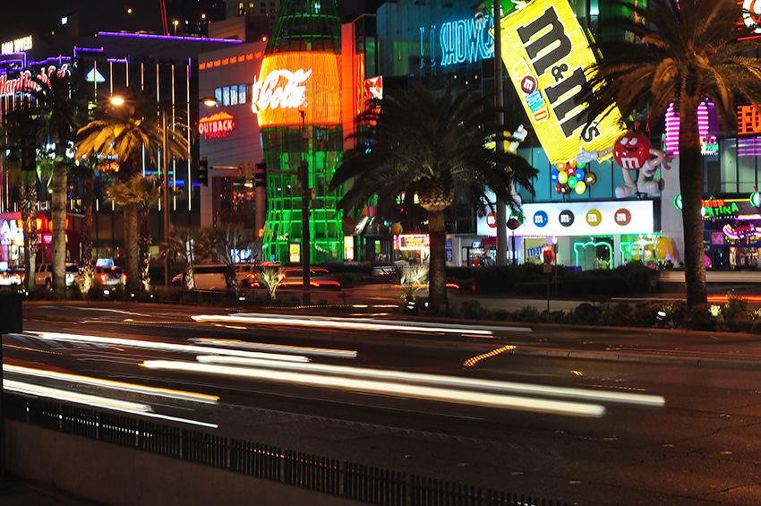 Neon signs and light-trail traffic along the Las Vegas Strip at night, with palm trees lining the street.