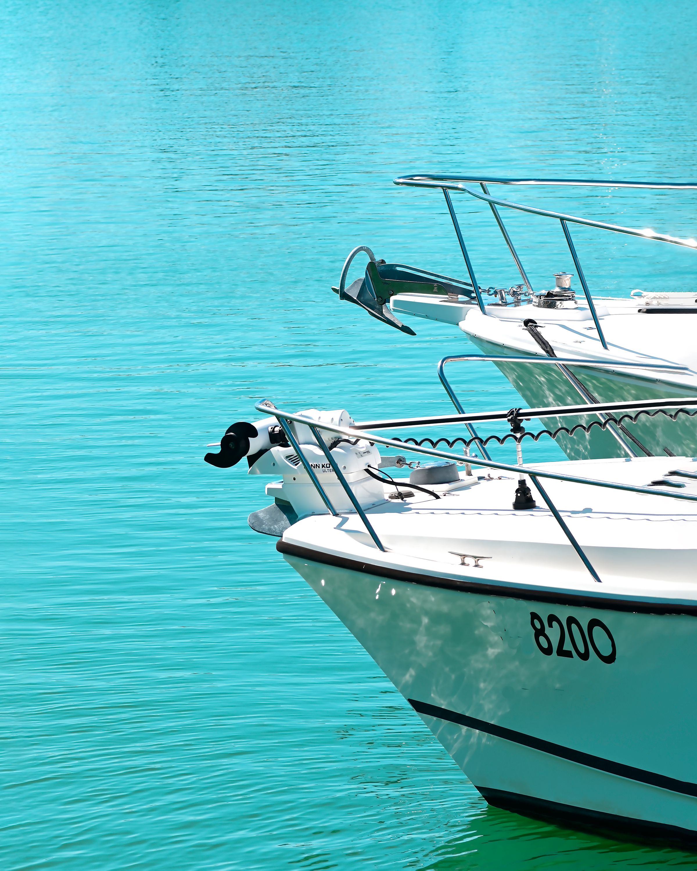 Two white boats moored bow-to-bow on turquoise water.