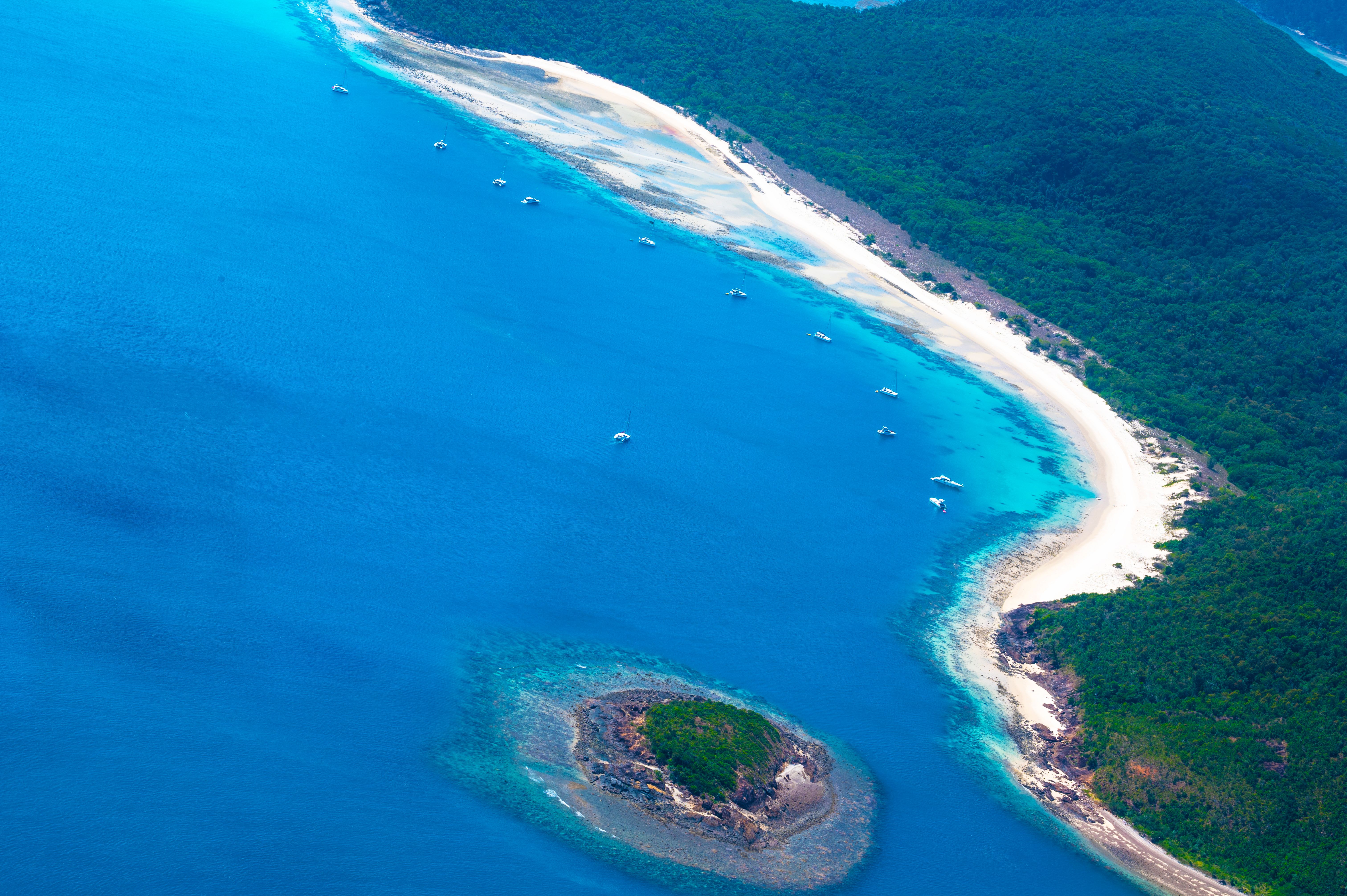 An aerial view of Whitehaven Beach's brilliant white sand and turquoise water, with yachts anchored along the shore.